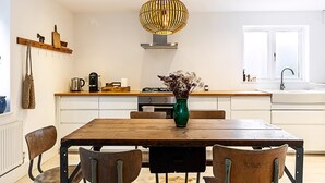 A modern kitchen with a wooden dining table, chairs, a hanging light fixture, and a vase with flowers.