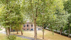A building with arched windows and a brick facade, surrounded by trees and a grassy area.