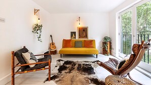 A modern living room with a yellow sofa, a wooden chair, a leather chair, a cowhide rug, and a guitar.