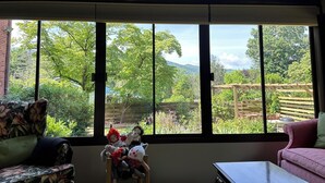 Quarto com uma janela grande, ventoinha no teto e uma cadeira de madeira com brinquedos de pelúcia.