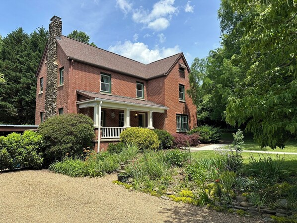 A two-story brick house with a stone chimney, a covered porch, and a well-maintained garden with various plants and shrubs.
