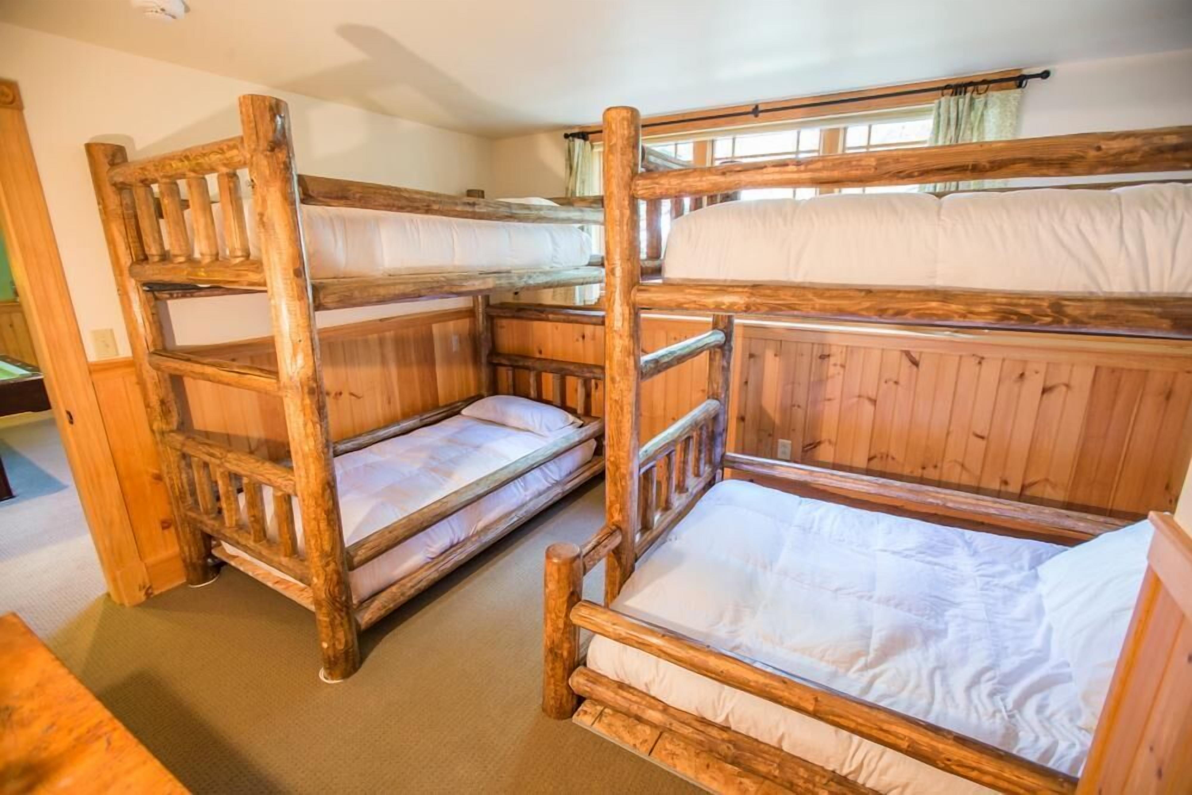 A room with two bunk beds made of wood, a wooden bench, and a window with curtains.