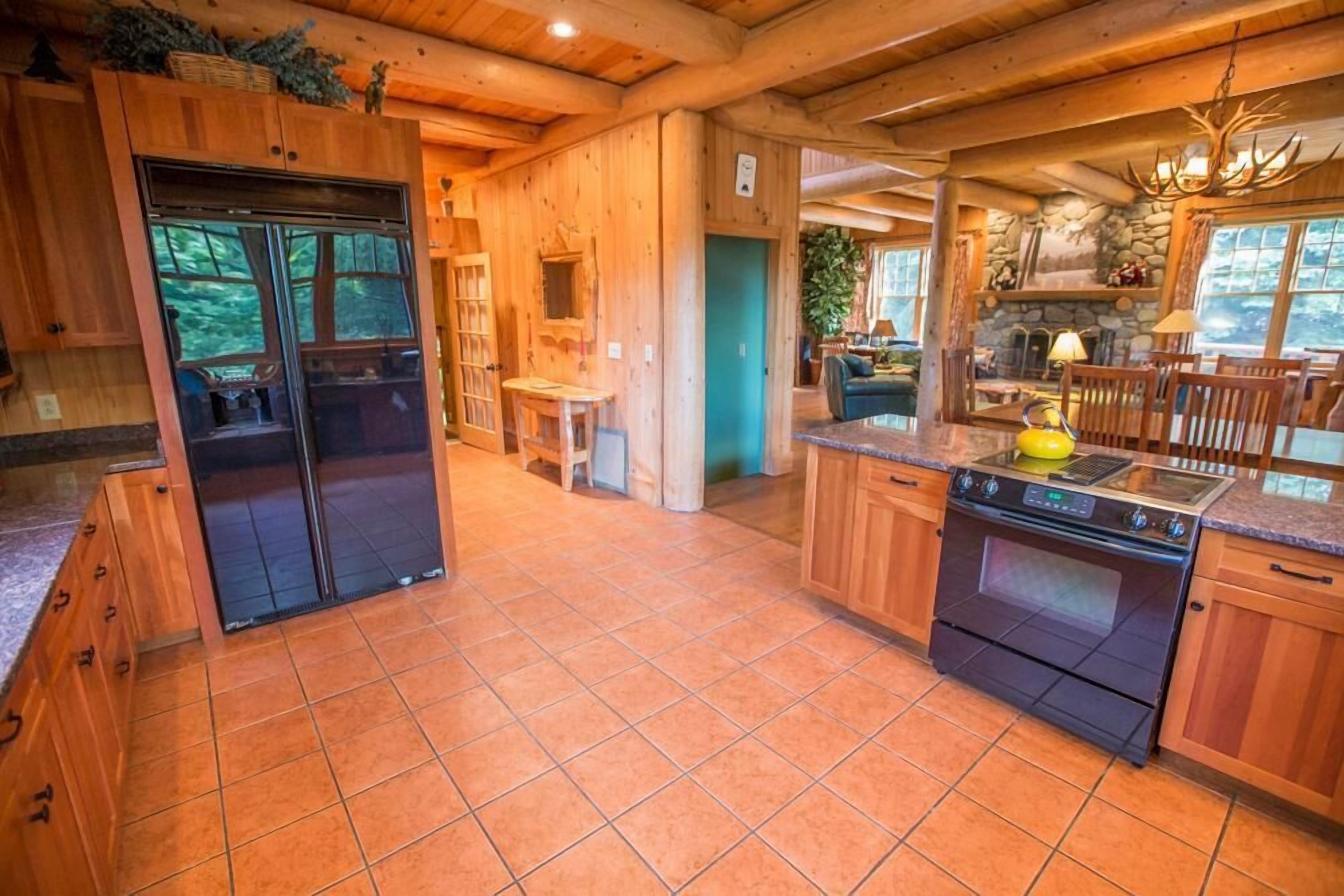 A wooden cabin interior with a kitchen, dining area, and a large window.