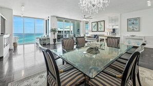 A spacious dining area with a glass table and striped chairs, a chandelier, and a view of the ocean. - Neptune's Niche 1122 managed by Destin Pointe Vacation Rentals (Destin)