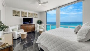 A bedroom with a large bed, a TV, a ceiling fan, and a view of the ocean. - Neptune's Niche 1122 managed by Destin Pointe Vacation Rentals (Destin)