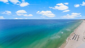 An aerial view of a beach with clear turquoise waters, a sandy shore, and a few people.