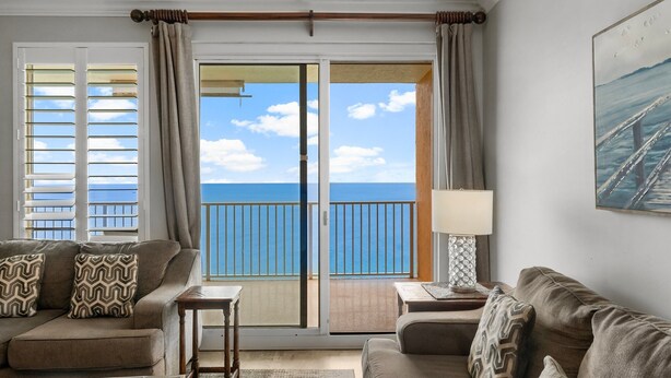 A living room with a sofa, a small table, and a view of the ocean through a sliding glass door.