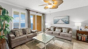 A living room with two sofas, a glass coffee table, a ceiling fan, a painting, and a bookshelf.