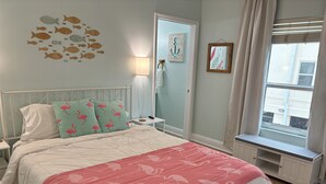 A neatly arranged bedroom with a bed, a nightstand, a lamp, a window with a view, and a wall with decorative elements.