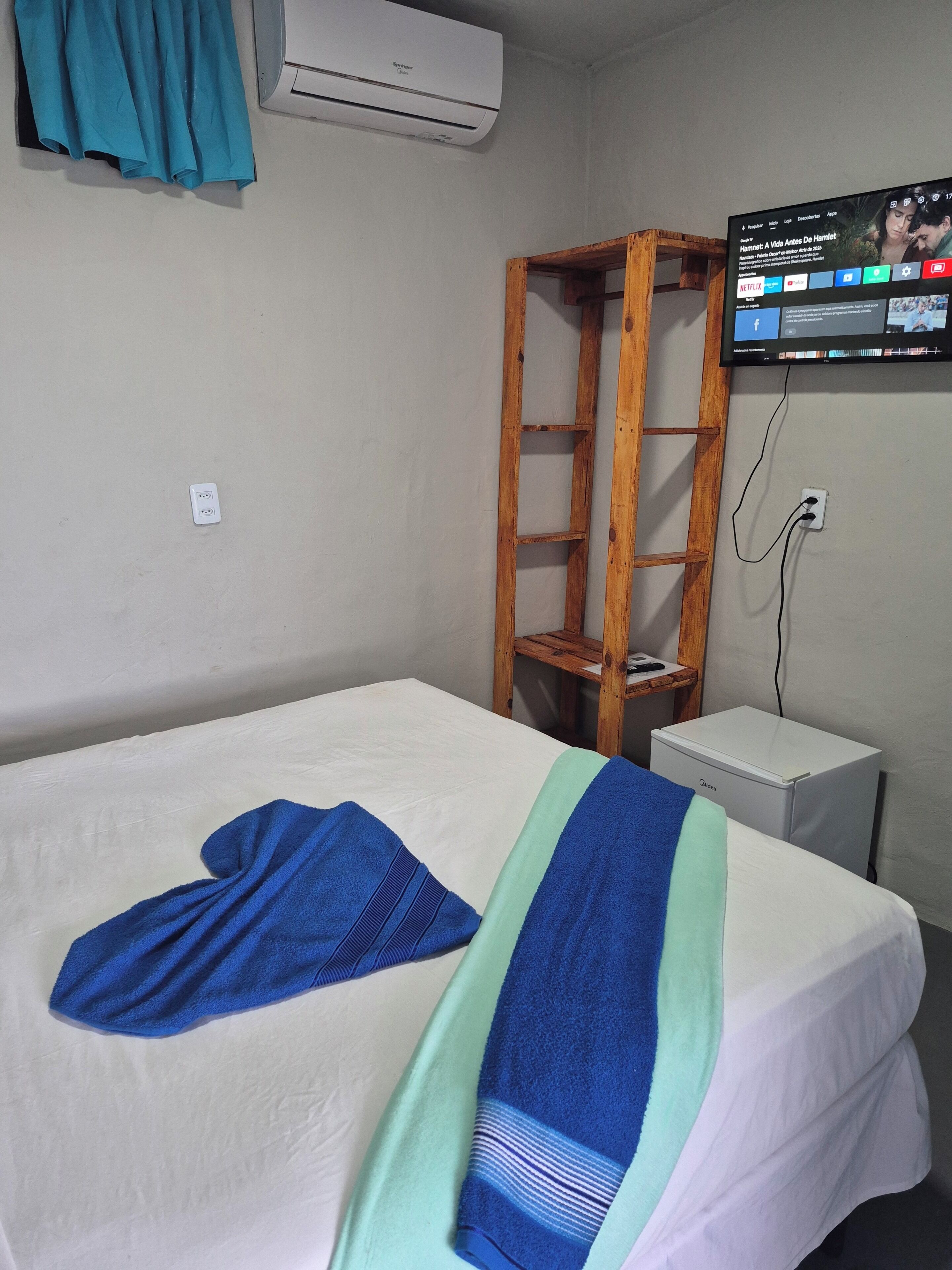 Una camera d'albergo con un letto, una scala in legno, un tavolino bianco e un condizionatore d'aria.