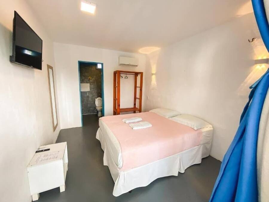 Un dormitorio con una cama, un televisor, una mesita y un equipo de aire acondicionado.