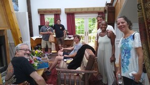 A group of people in a room with a fireplace, a dining table, and a window with curtains. - Mountain, Lake & Babbling Brook Retreat (Newbury)