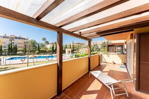 Ein Balkon mit Blick auf einen Swimmingpool, eine Liege und ein Gebäude mit einem Ziegeldach.