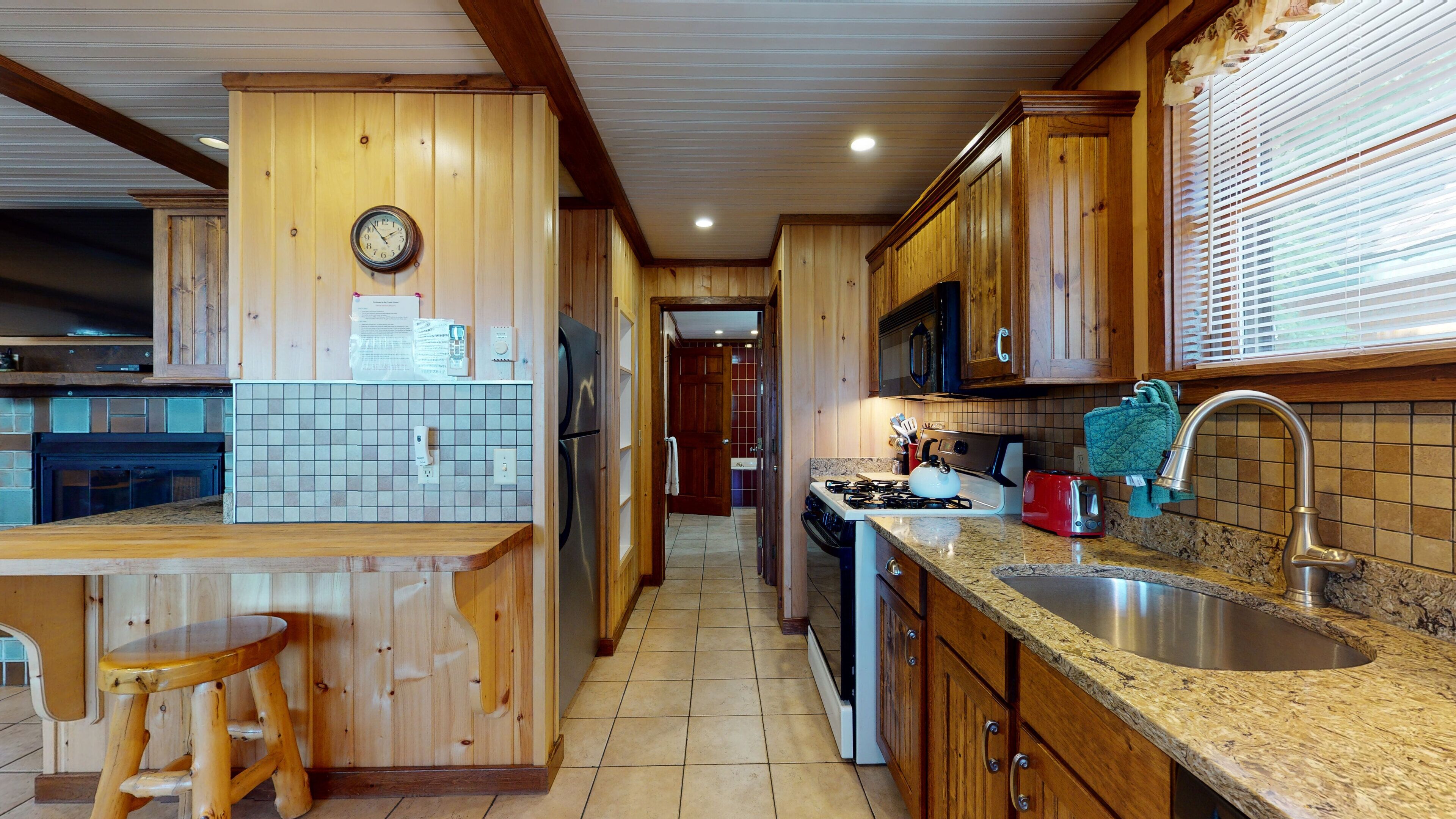 Una cocina con armarios de madera, encimera de granito, pileta de acero inoxidable y estufa.