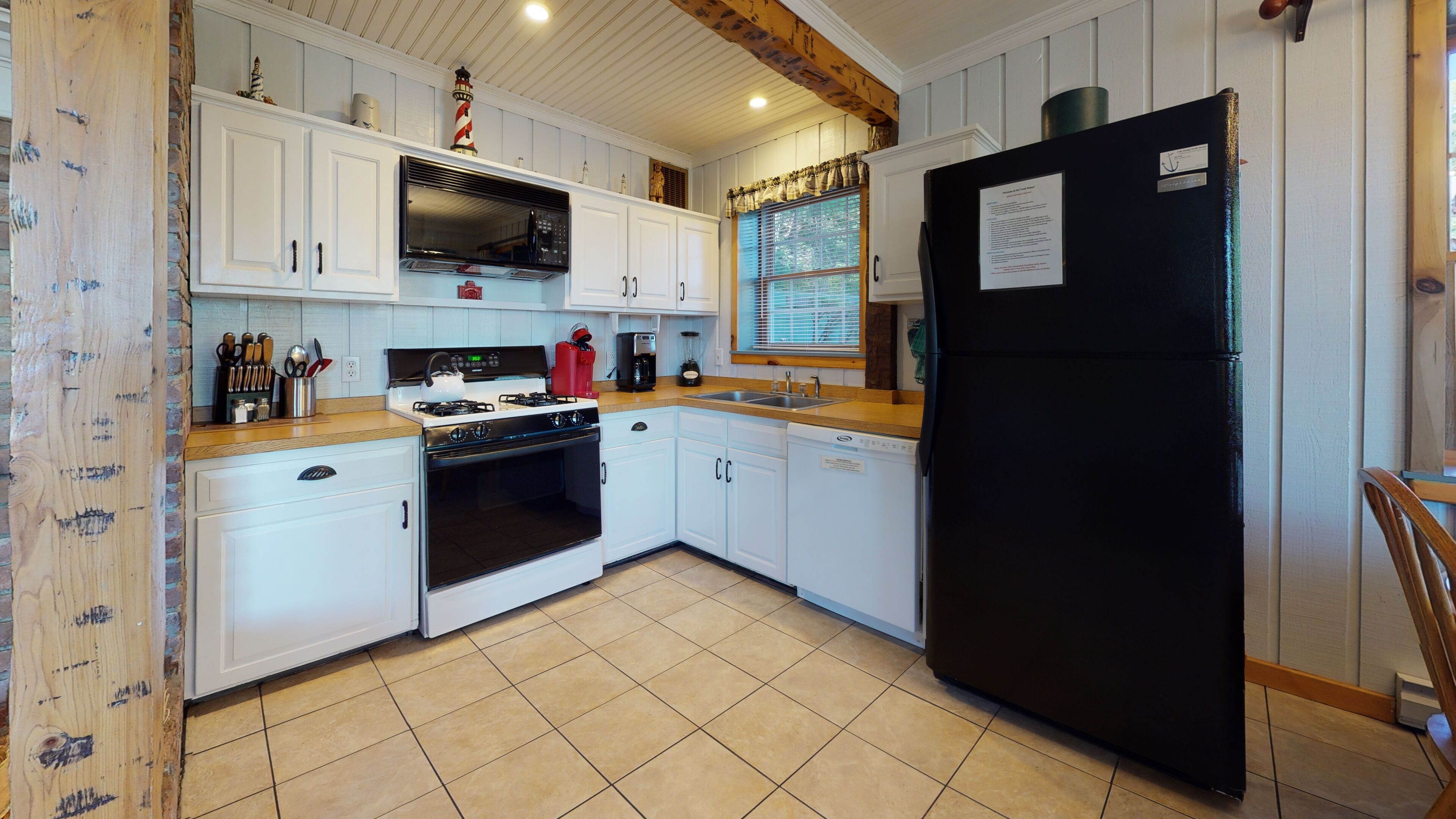 A kitchen with white cabinets, a black refrigerator, a stove, and a window with blinds.