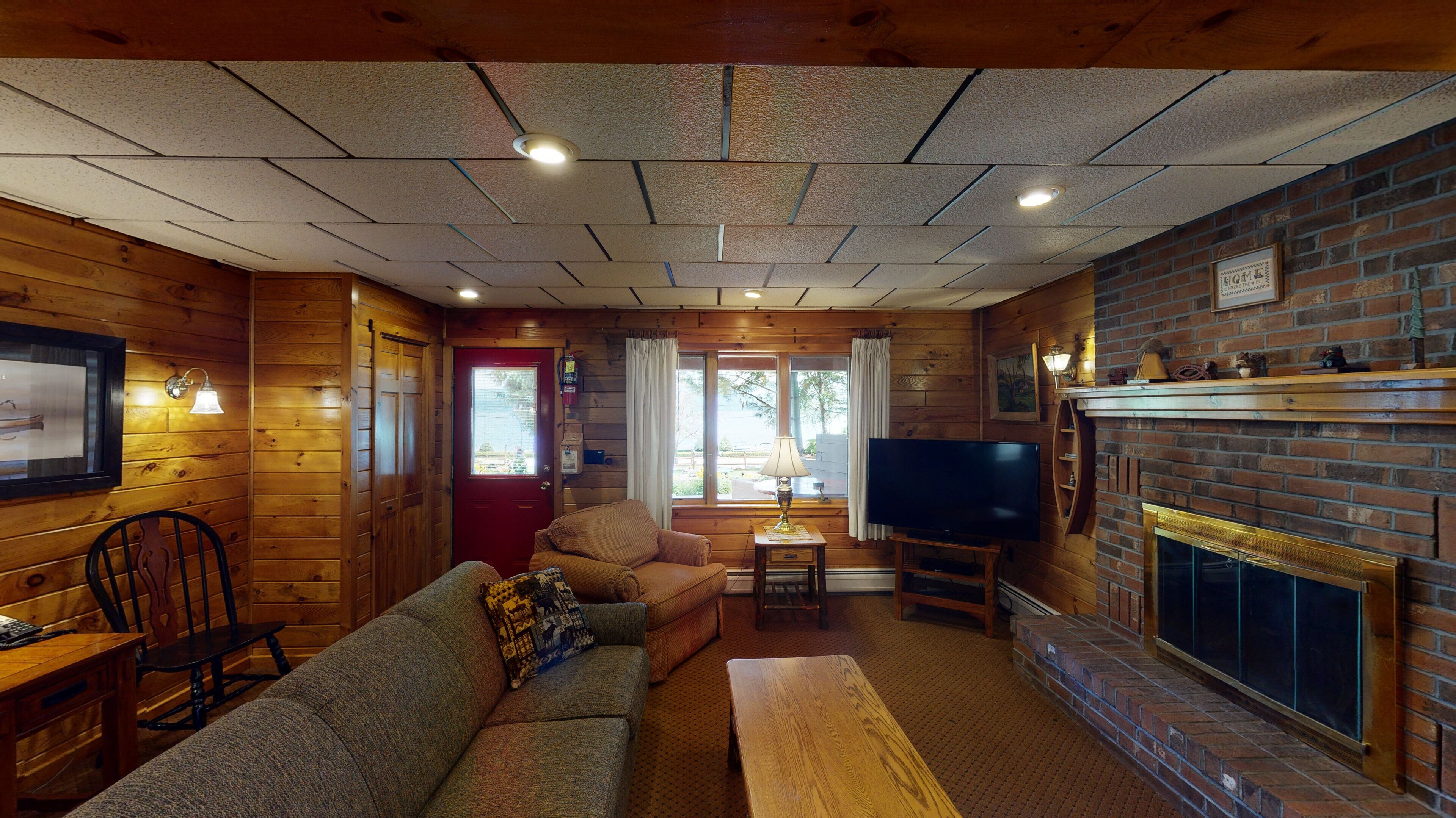 A cozy cabin interior with a wooden interior, a fireplace, a television, and a sofa.