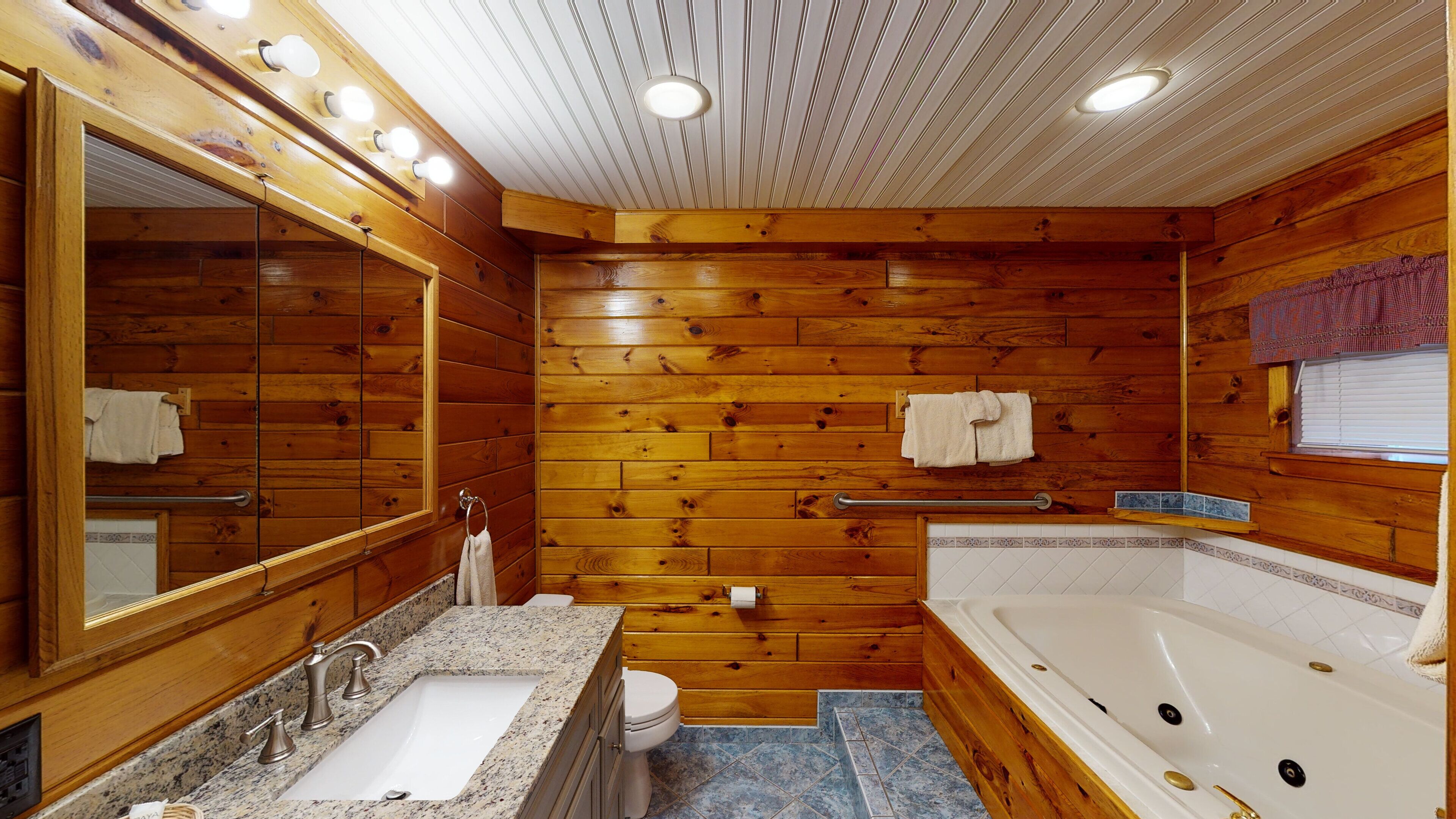 A wooden bathroom with a large mirror, a sink, a toilet, and a bathtub.