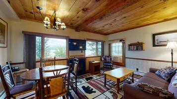 Una sala de estar acogedora con techo de madera, chimenea, comedor con sillas de madera, sofá y televisor montado en la pared.