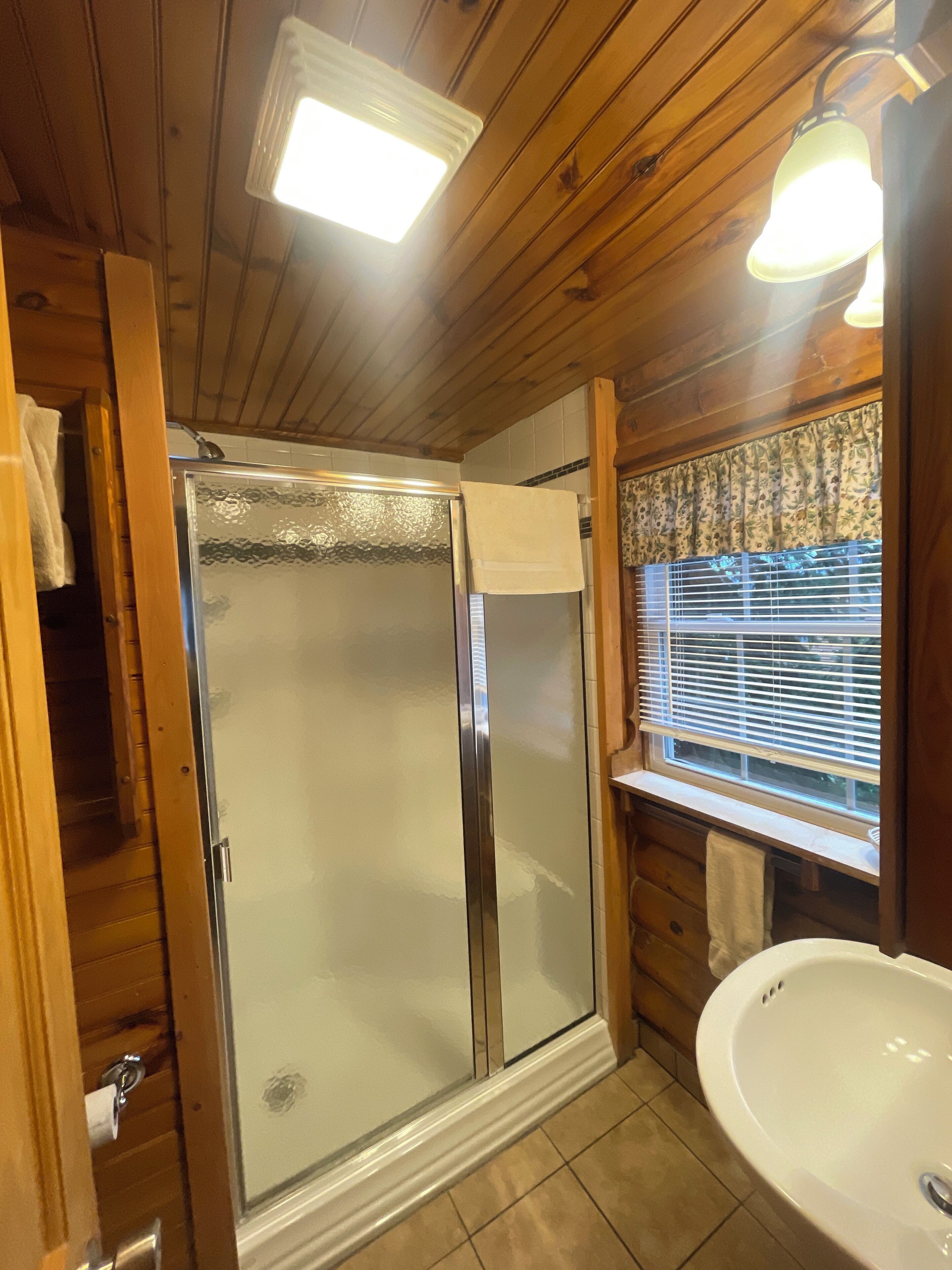 A bathroom with a glass-enclosed shower, a sink, and wooden paneling.