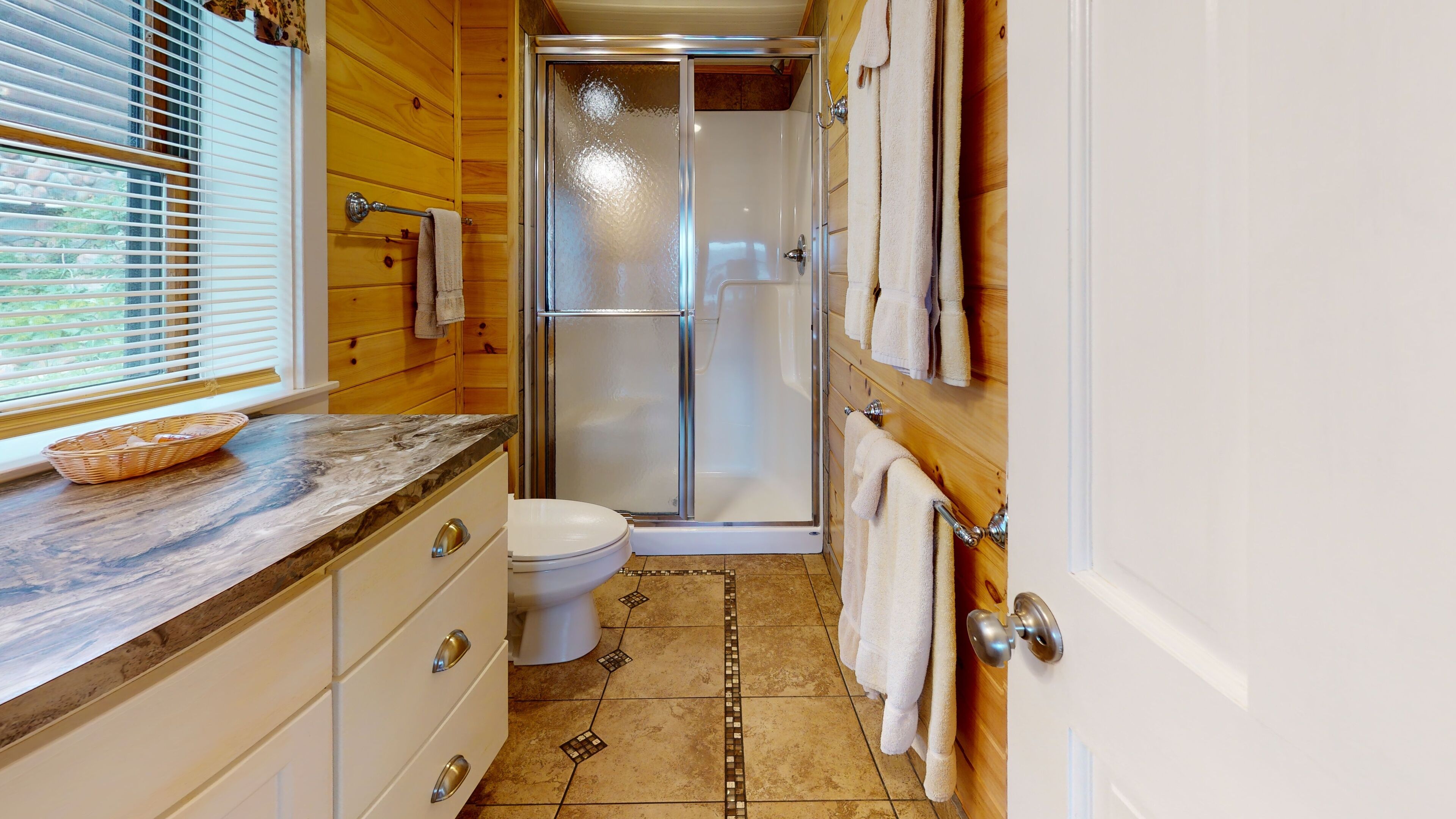 A compact bathroom with a shower, toilet, and a sink with a marble countertop.