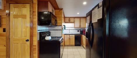 Una cocina con armarios de madera, un refrigerador negro, una estufa y un microondas.