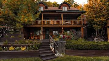 A two-story log cabin with a balcony, surrounded by a landscaped garden with steps leading to the entrance.