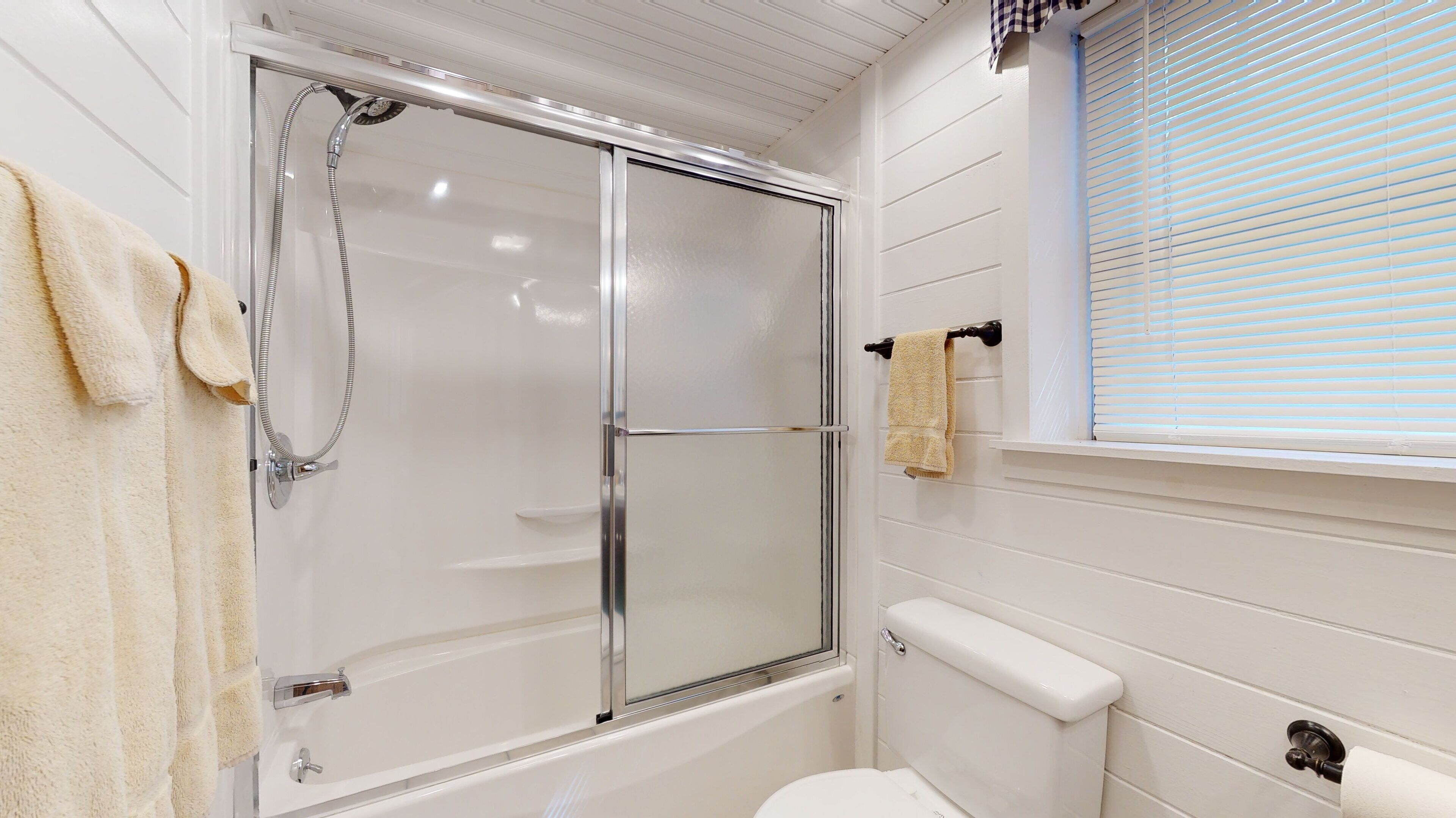 Une salle de bain avec une douche en verre, des toilettes et une fenêtre avec des stores.
