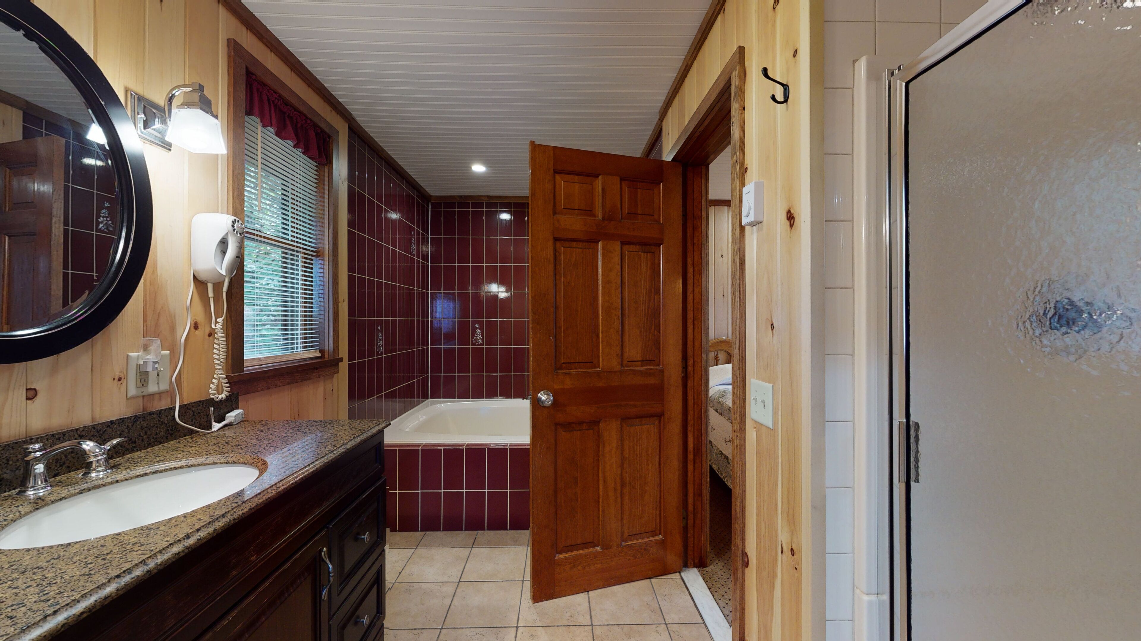 A bathroom with a wooden vanity, a round mirror, a hairdryer, and a bathtub.