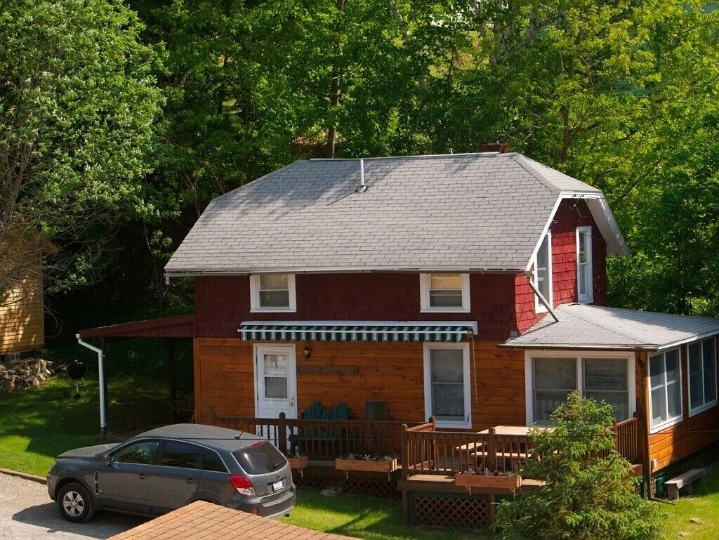 A two-story house with a porch, a car parked in front, and a well-maintained lawn.