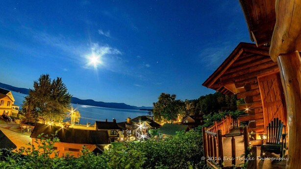 Una cabaña junto al lago con una terraza de madera y vistas al lago.