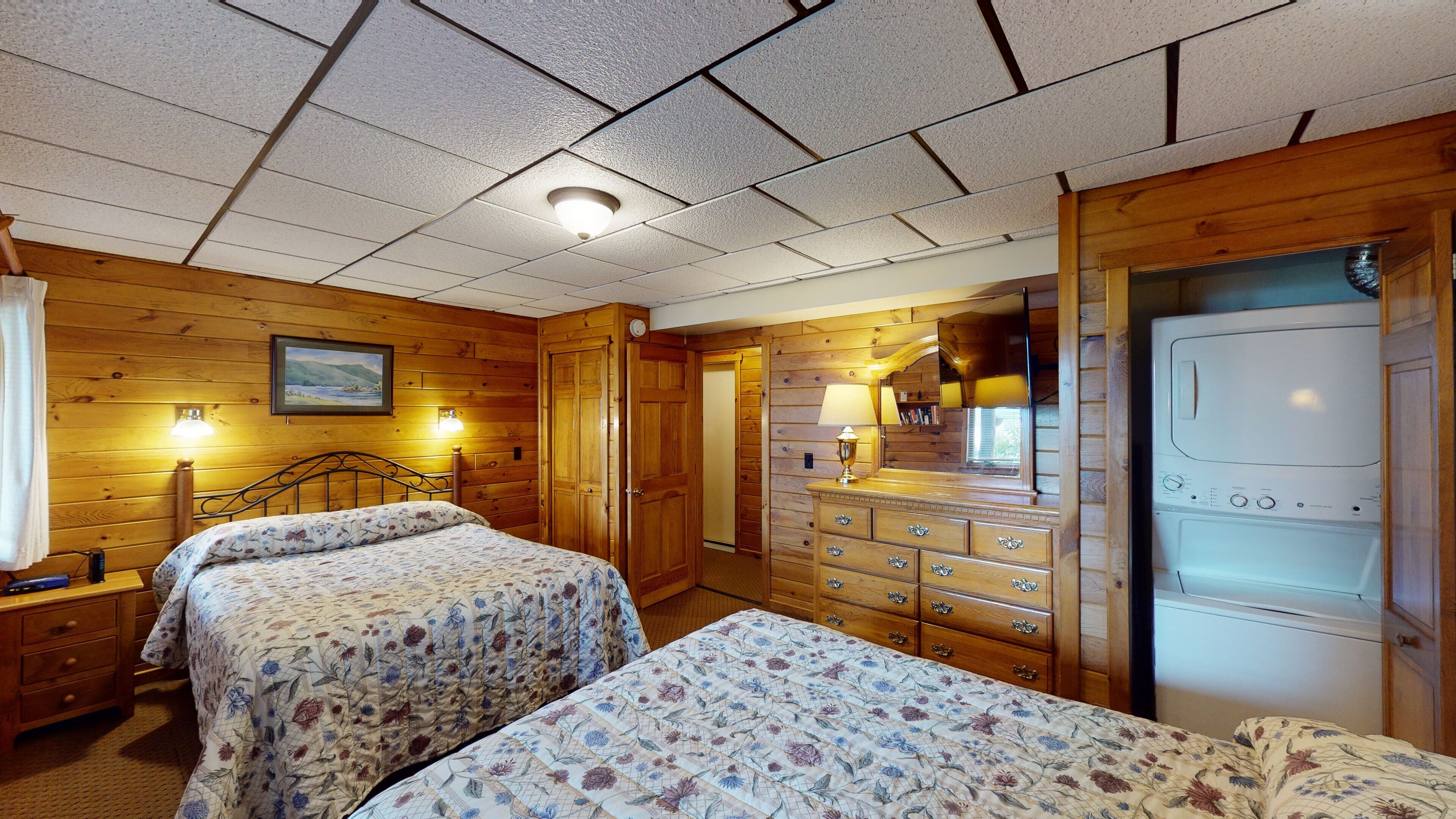 A room with two beds, wooden walls, a dresser, and a washing machine.