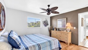 Ein Schlafzimmer mit Bett, Schminktisch, Deckenventilator, Fenster mit Ausblick und einer Tür.
