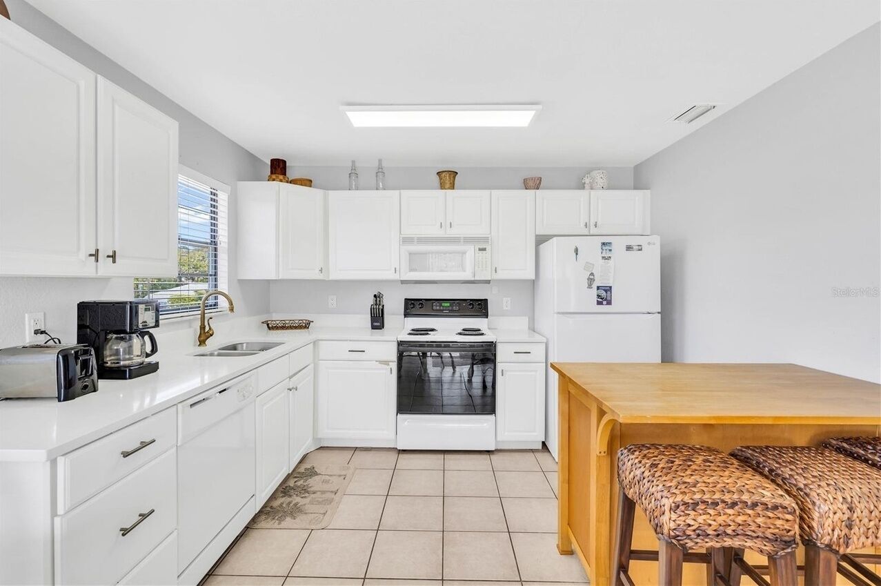 A kitchen with white cabinets, a microwave, a stove, a refrigerator, a wooden table, and two woven stools.