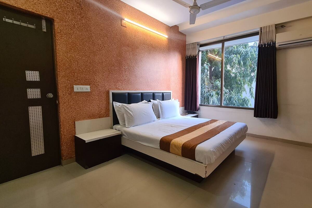 Une chambre d’hôtel comprenant un lit, une table de chevet, une fenêtre avec des rideaux, un appareil de climatisation et une porte avec une serrure.