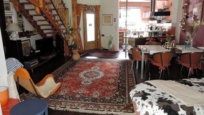 Amplia sala de estar con un tapete grande, un sofá, una mesa de comedor con sillas, una cocina al fondo y una escalera.