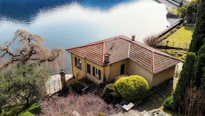 A house with a tiled roof, a small garden, and a view of a lake. - Villa Vica (Musso)