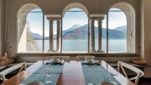 A dining area with a view of a lake and mountains, featuring a long table set with plates and glasses. - Villa Vica (Musso)
