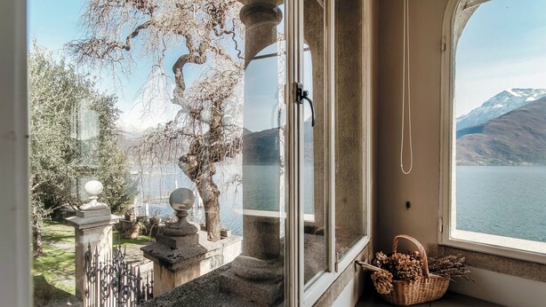 A room with a large window overlooking a lake and mountains. There is a wicker basket on the windowsill. - Villa Vica (Musso)