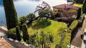 A house with a red roof surrounded by a well-maintained garden and a view of a lake. - Villa Vica (Musso)
