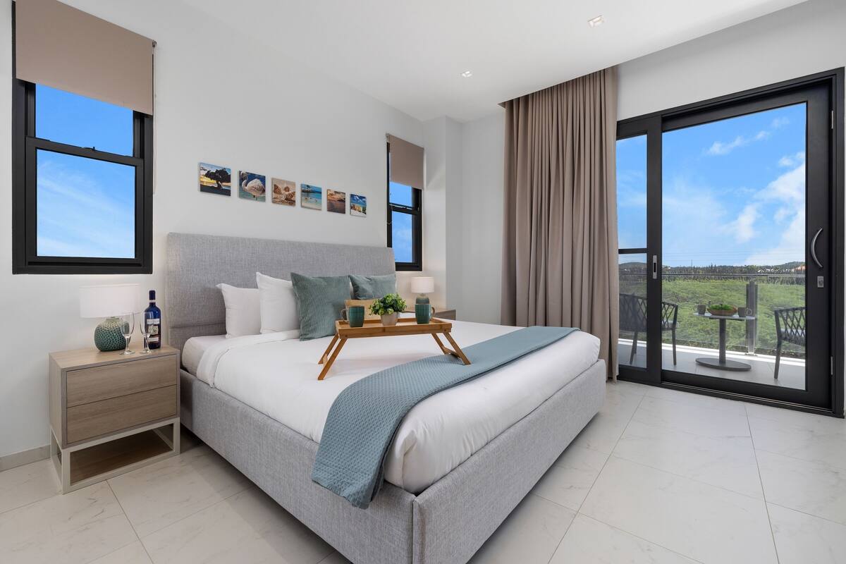 Ein modernes Schlafzimmer mit einem großen Bett, Nachttischen, einem Fenster und einem Balkon mit Blick.