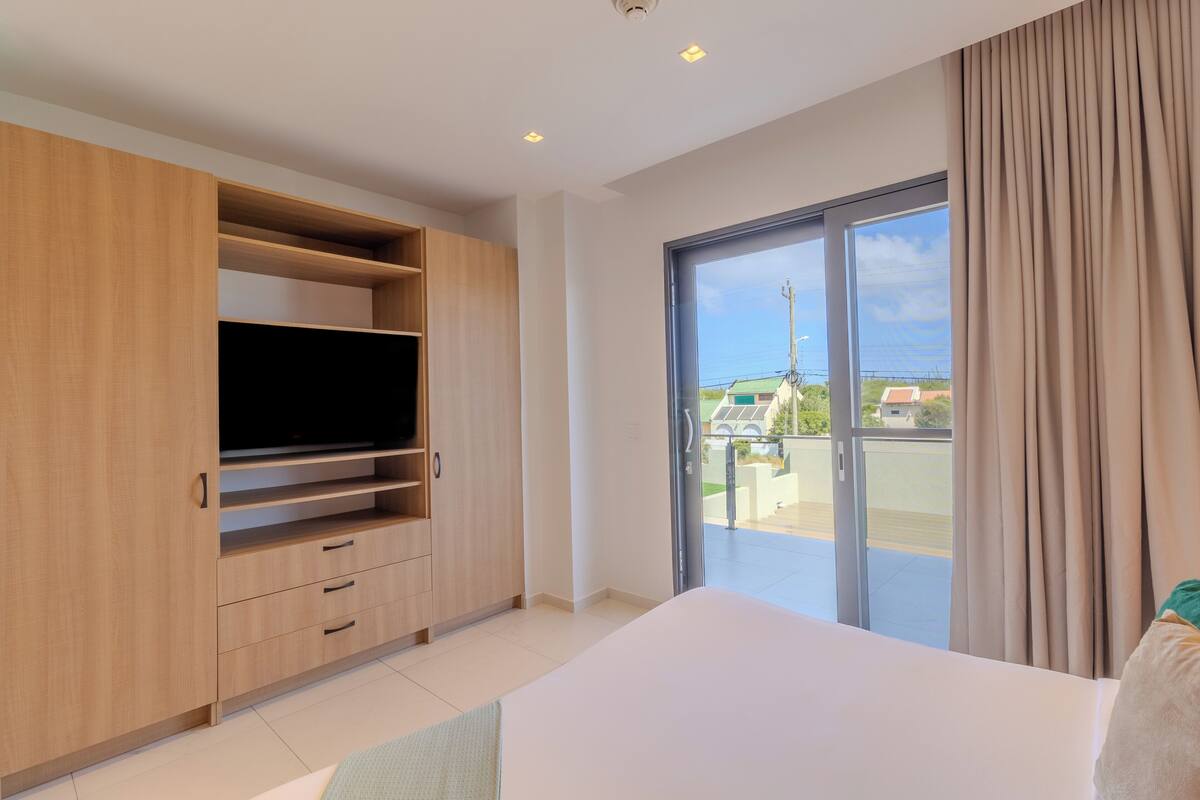 Ein modernes Schlafzimmer mit einem großen Bett, einem eingebauten Holzschrank, einem Flachbildfernseher und einer Glastür, die auf einen Balkon führt.