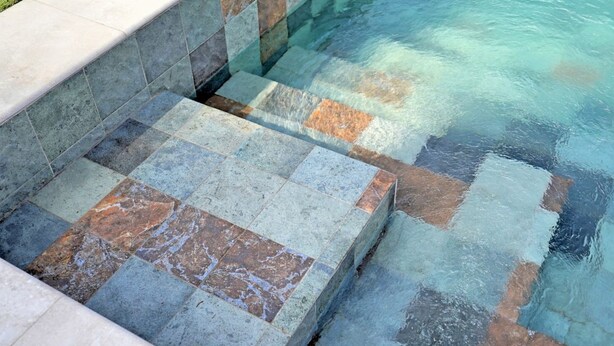Ein Pool mit klarem Wasser, aus dem heraus Steinstufen führen, und ein gefliestes Beckenrand.