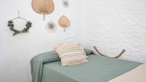 Ein Bett mit grüner Bettdecke und einem Zierkissen, eine Wand mit strukturierter Oberfläche und Wanddekorationen, darunter ein Ventilator und ein Kranz.