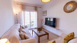 Una sala de estar con un sofá, una mesa de centro, un televisor y una ventana con cortinas.