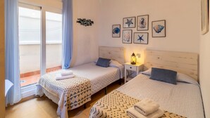 Una habitación con dos camas, una mesita pequeña y una pared decorada con cuadros.