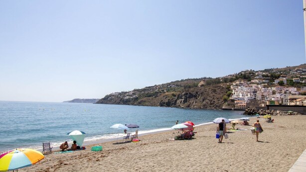 Una playa con sombrillas, gente y edificios al fondo.