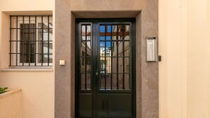 Una puerta negra con un ventanal encima, un buzón pequeño a la derecha y un suelo de baldosas.