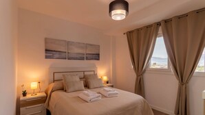 A neatly arranged bedroom with a bed, bedside lamps, a nightstand, and a view of the outdoors through curtains.
