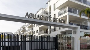 A modern apartment building with balconies, a gated entrance, and the name "AGUACATE BEACH" displayed above the entrance.