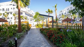 A pathway leading to a covered area with palm trees and flower beds.